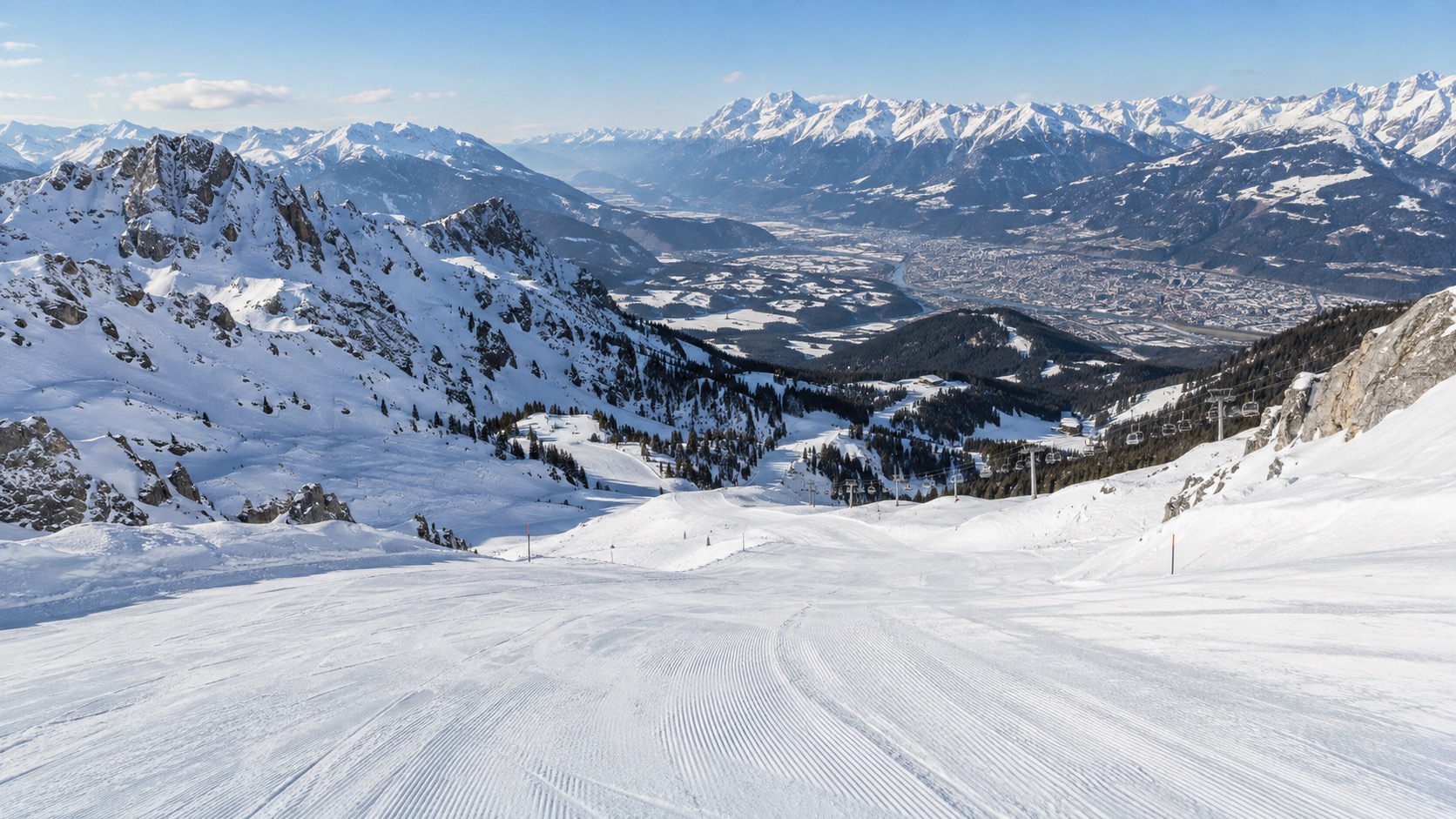 Wide groomed red run at Axamer Lizum with the Innsbruck valley visible in the distance